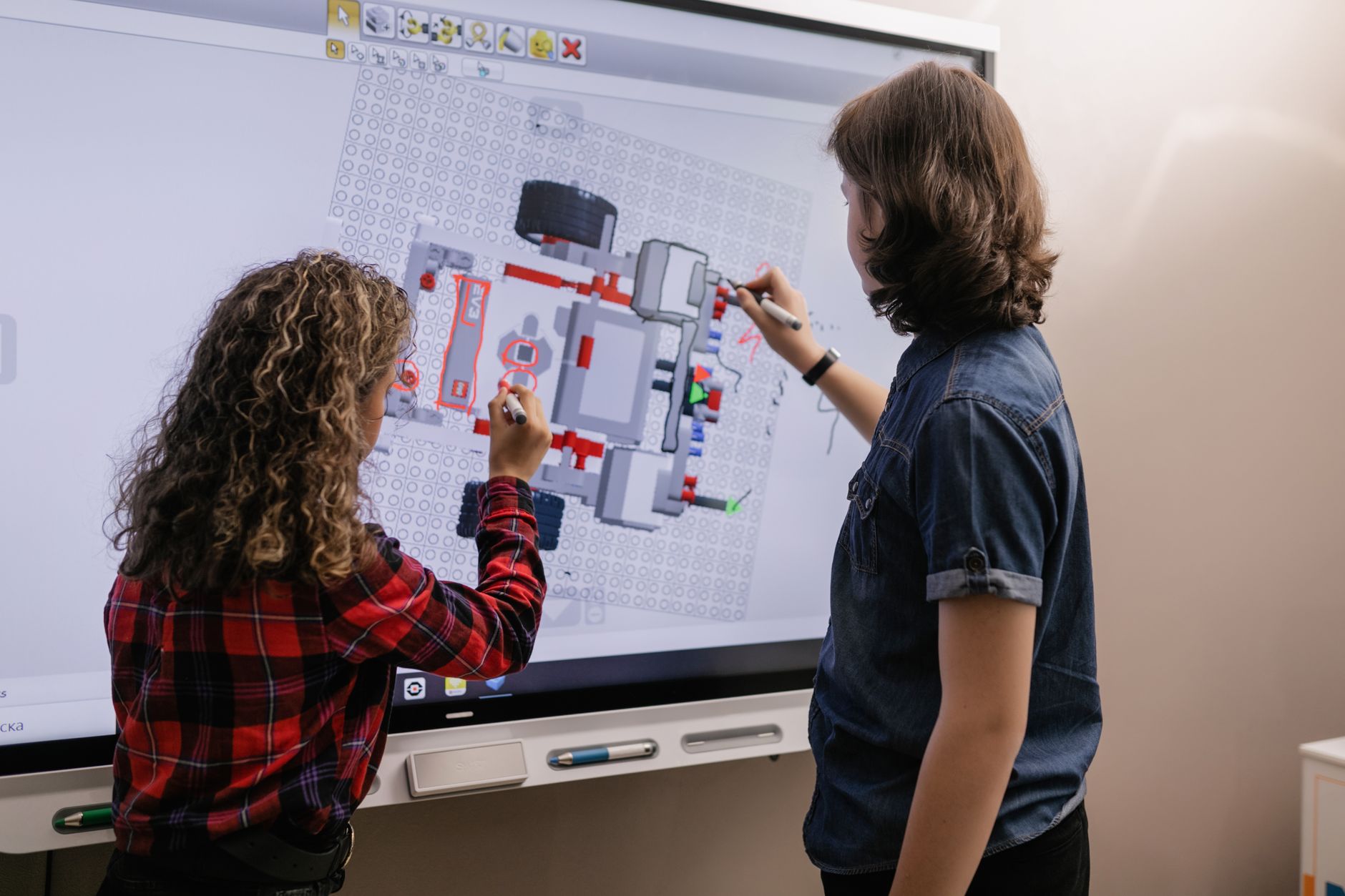 Enseignant et élèves réunis autour d’un écran interactif tactile dans une salle de classe lumineuse, avec un schéma pédagogique annoté et plusieurs élèves participant à l’activité.