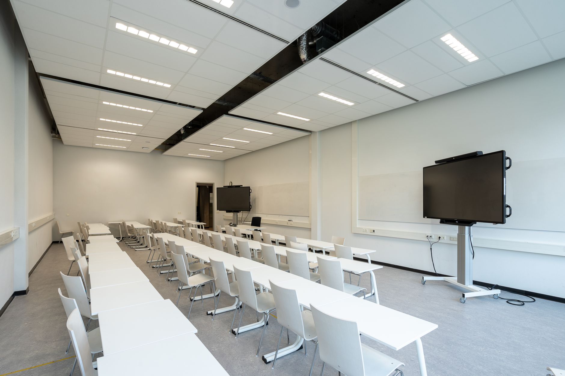 Vue latérale d’une salle de classe montrant la distance de lecture, la hauteur d’installation de l’écran et la disposition des tables face à la surface tactile.